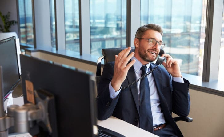 Businessman Making Phone Call Sitting At Desk In Office